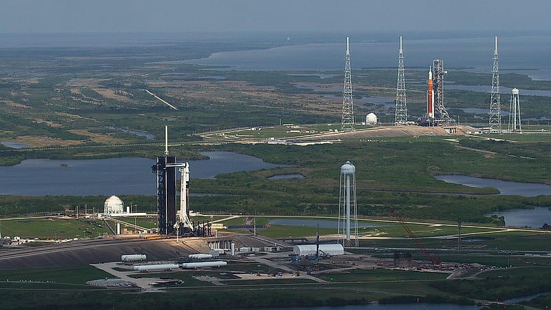 A tall white rocket standing against a metal service tower at dawn with vapor drifting from its side.