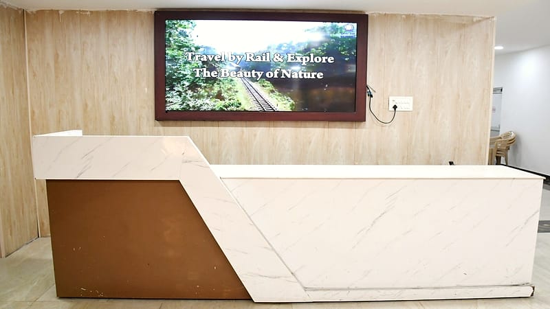An empty office reception area with a visitor sign-in tablet, a lanyard on the desk, and glass doors behind.