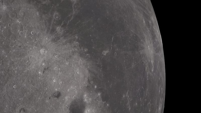 A gray cratered rock surface photographed at low angle with long shadows and fine dust covering scattered stones.