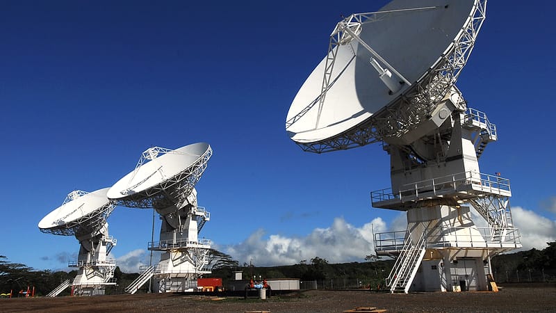 A row of large white parabolic dish antennas on concrete pads pointing at a clear sky above dry grassland.