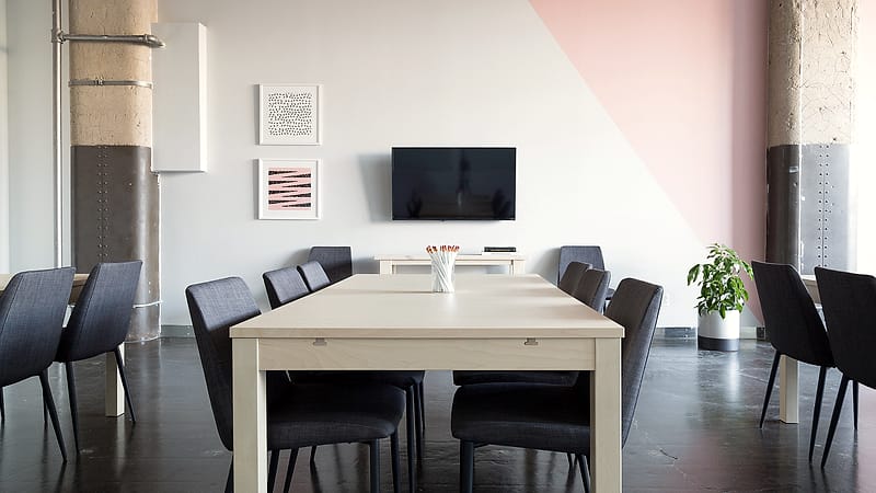A plain conference room with a long table, folding chairs, a recording microphone and closed blinds on the window.