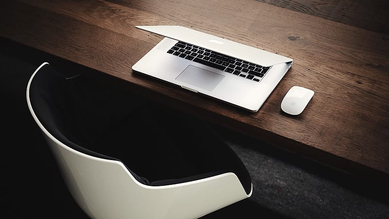 An empty chair pushed back from a long conference table, with a half-full water glass and a closed notebook.