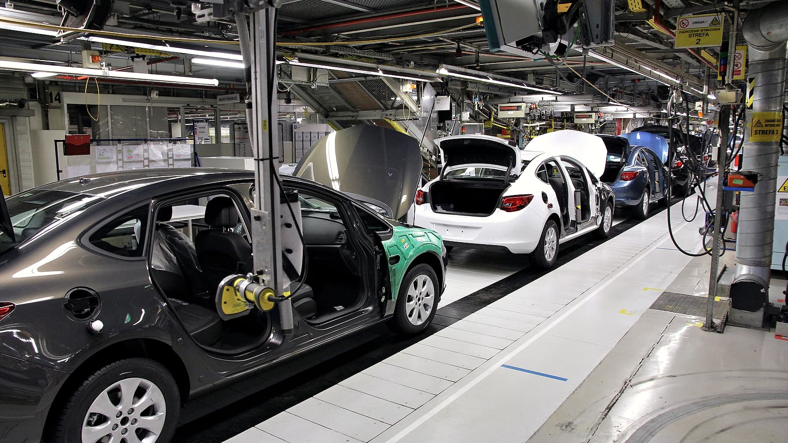 Workers at a long assembly bench fitting small metal components into housings under bright overhead lamps.